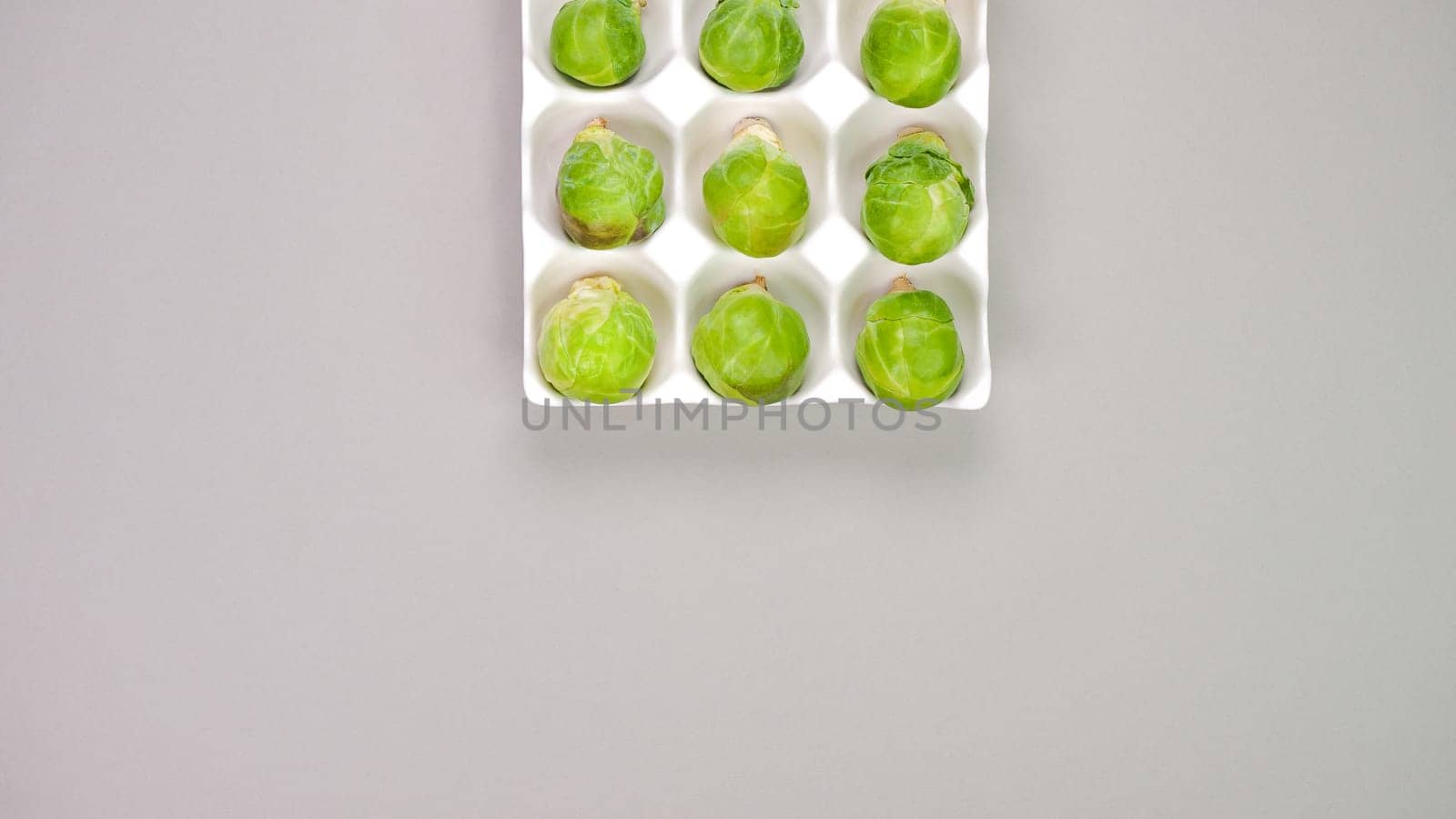 Raw organic Brussel sprouts in yellow white egg container on grey background, top view. Flat lay, overhead, from above. Copy space by JuliaDorian