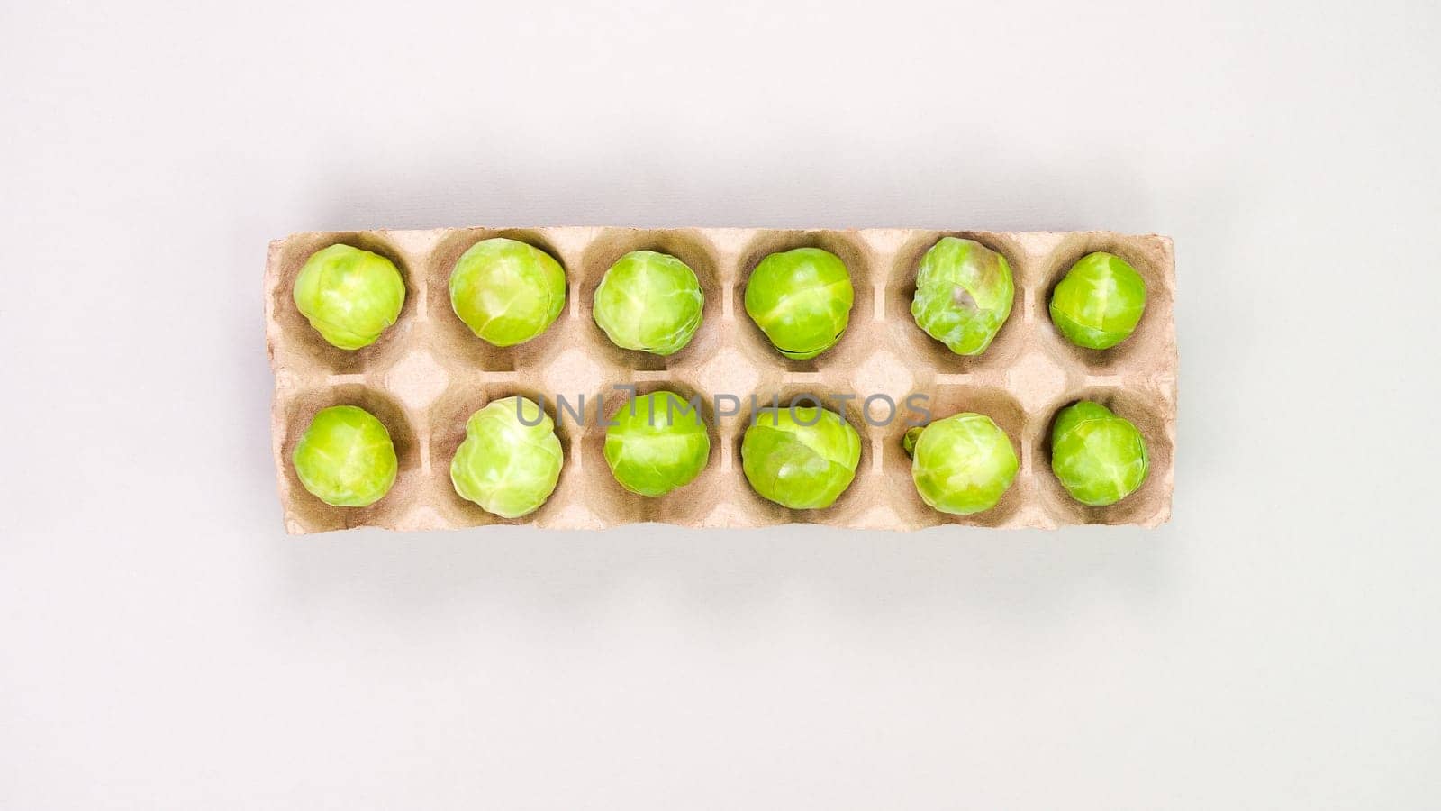 Raw organic Brussel sprouts in brown egg container on grey background, top view. Flat lay, overhead, from above. Copy space. by JuliaDorian