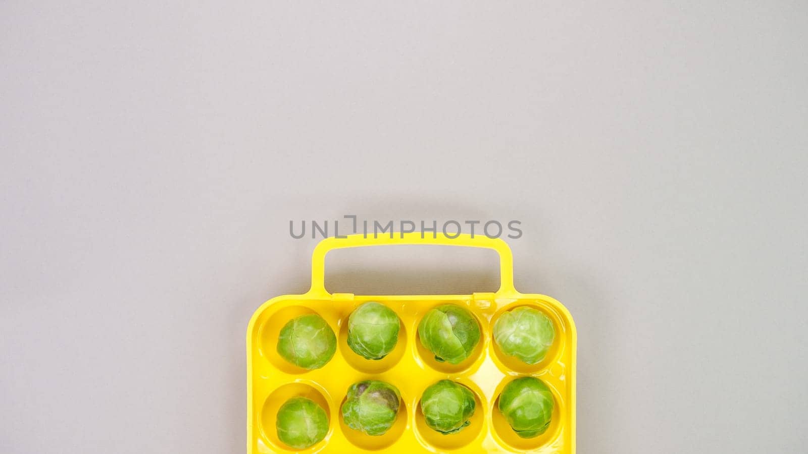 Raw organic Brussel sprouts in yellow container on grey background, top view. Flat lay, overhead, from above. Copy space