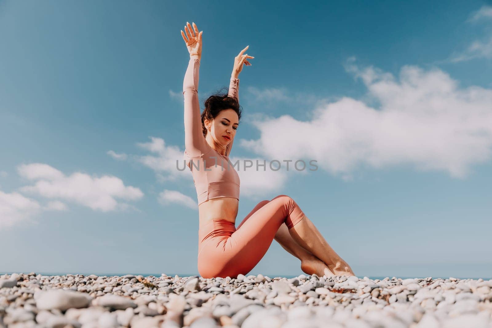 Middle aged well looking woman with black hair, fitness instructor in leggings and tops doing stretching and pilates on yoga mat near the sea. Female fitness yoga routine concept. Healthy lifestyle by panophotograph