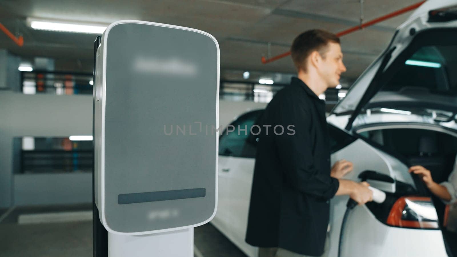 Young couple travel with EV electric car to shopping center parking lot charging in downtown city showing urban sustainability lifestyle by green clean rechargeable energy of electric vehicle innards