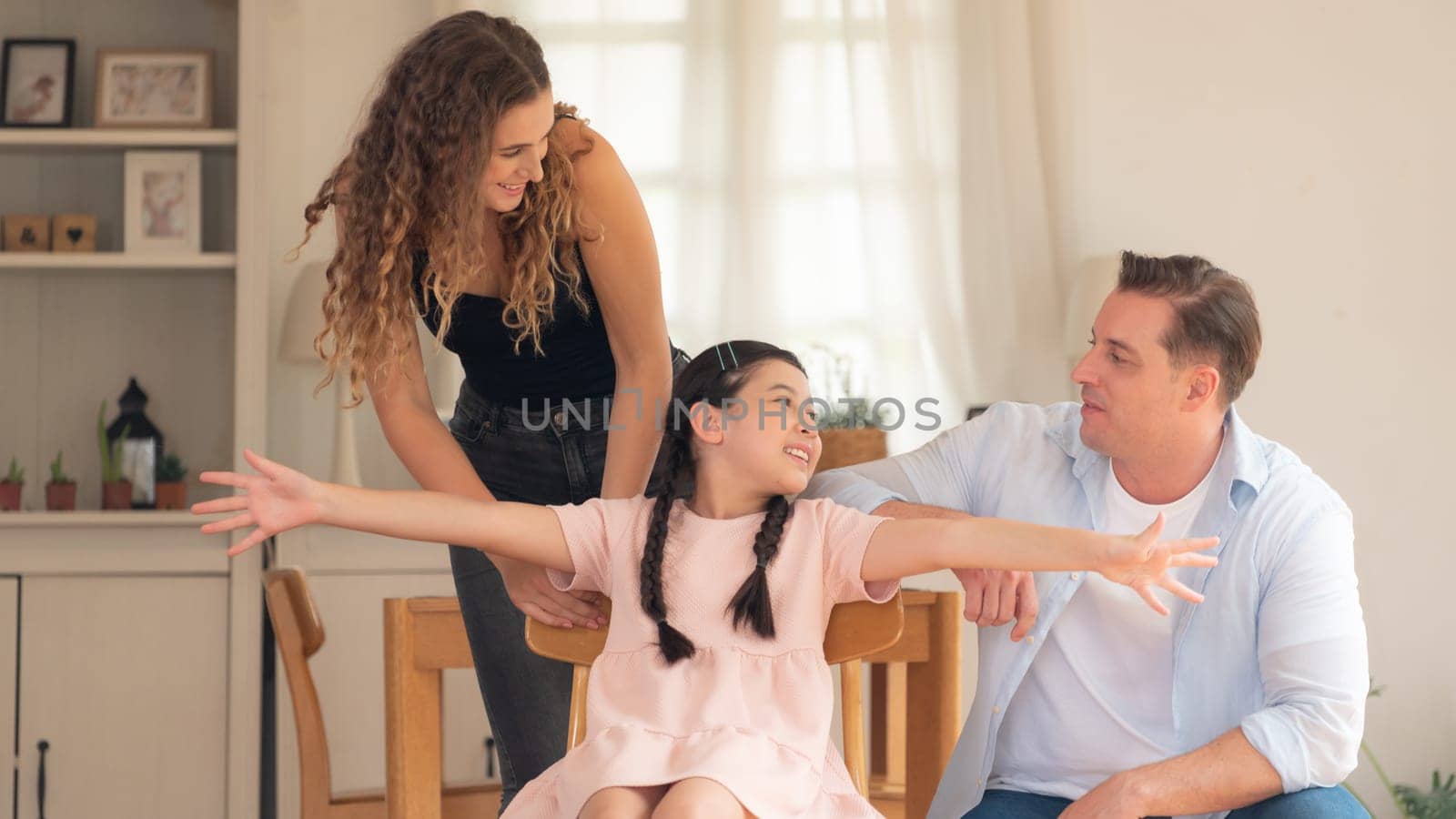 Happy family portrait with lovely little girl smile and looking at camera, lovely and cheerful parent and their daughter sitting together in living room at home with warm daylight. Panorama Synchronos