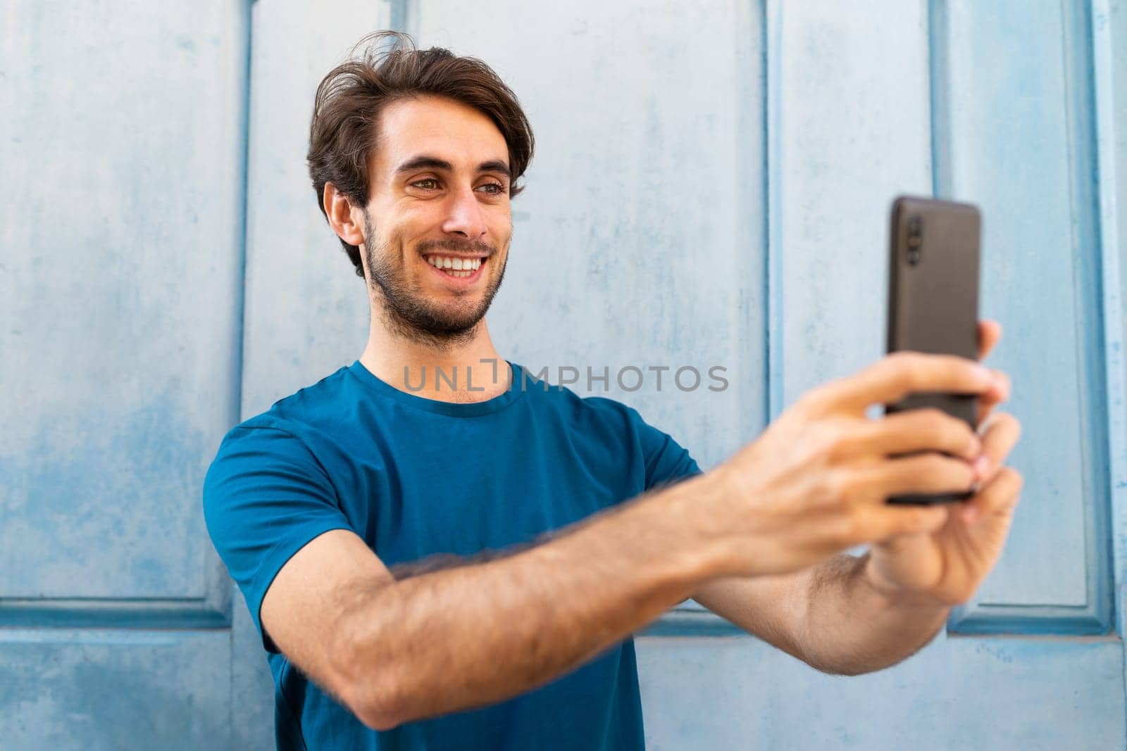 Young caucasian man taking a selfie using mobile phone outdoors. by Hoverstock