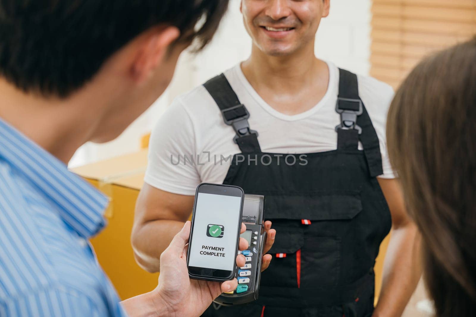 Post-moving couple scans QR code to pay via smartphone. Worker holds a box. Professional movers ensure quality home relocation. Business and industry shown. Online payment for moving