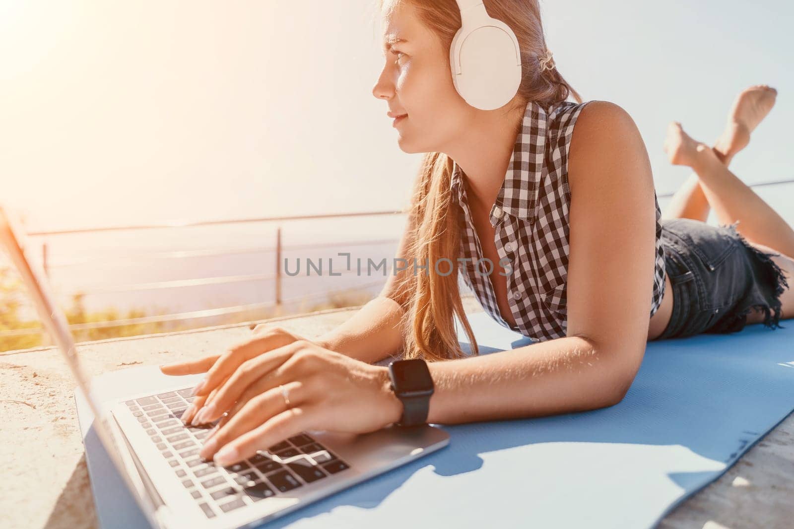 Digital nomad, Business woman working on laptop by the sea. Pretty lady typing on computer by the sea at sunset, makes a business transaction online from a distance. Freelance, remote work on vacation