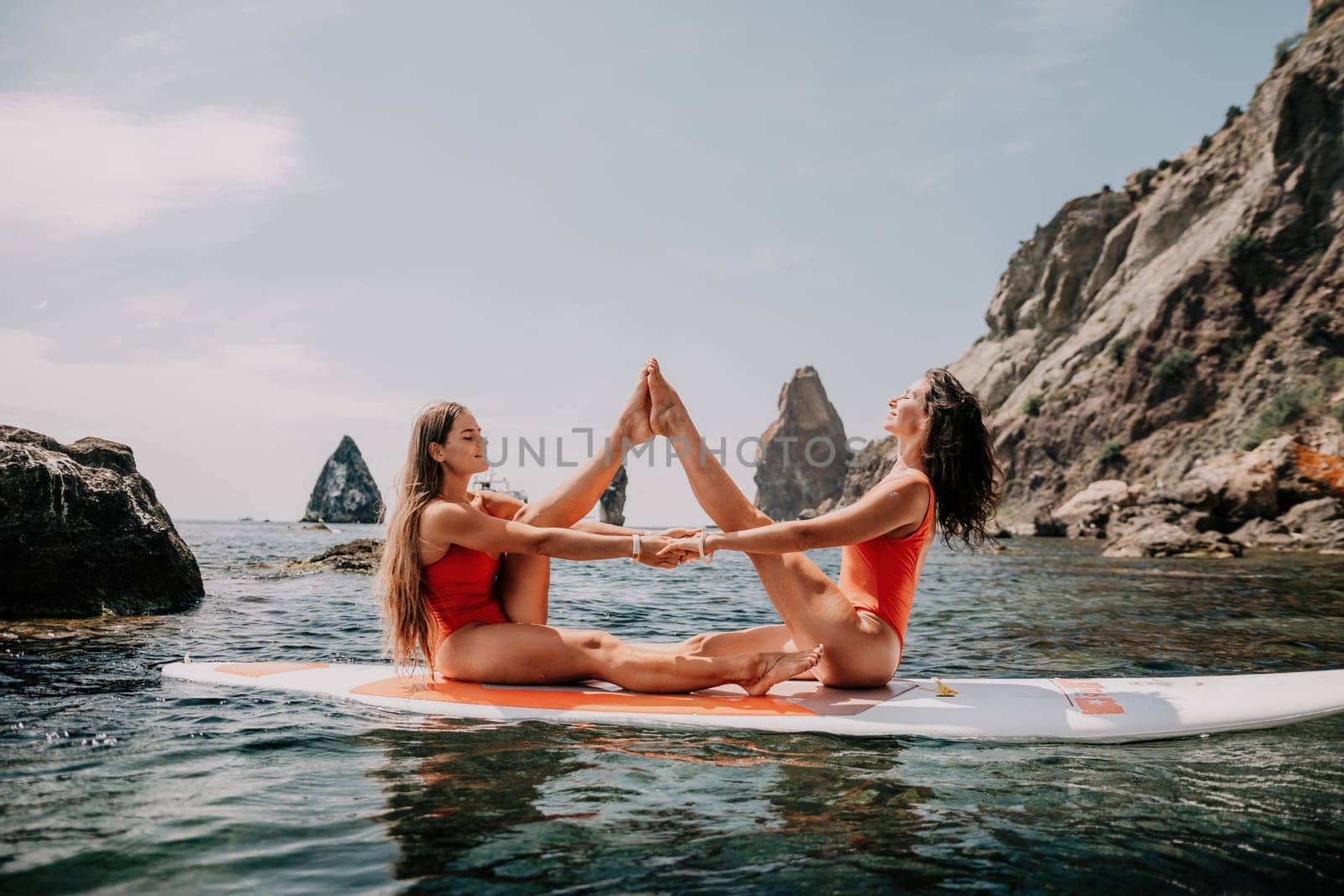 Woman sup yoga. Two happy sporty women practising yoga pilates on paddle sup surfboard. Female stretching doing workout on sea water. Modern individual female hipster outdoor summer sport activity. by panophotograph
