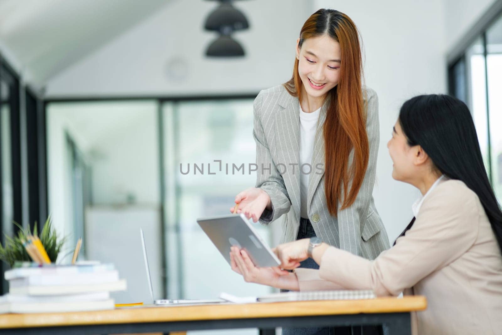 Office woman is standing and teaching a new employee. It describes the work format displayed on the tablet screen.