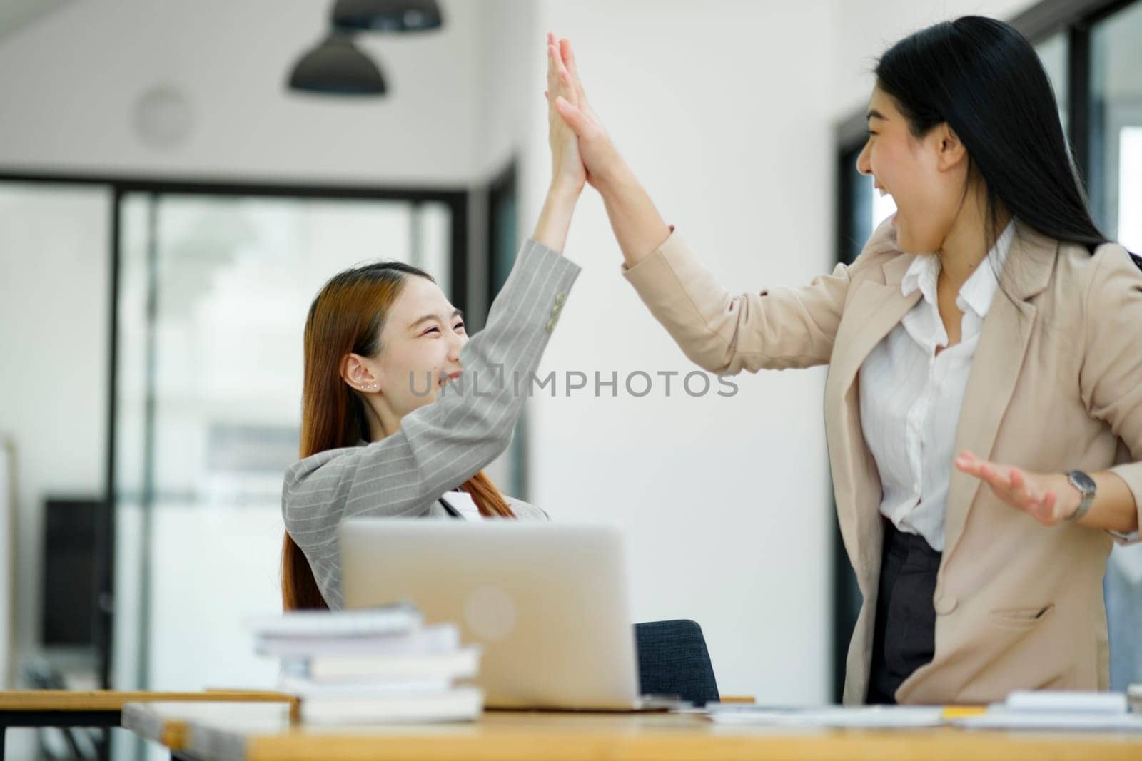 Two women are high-fiving with joy at their success in business and celebrate performance and teamwork..