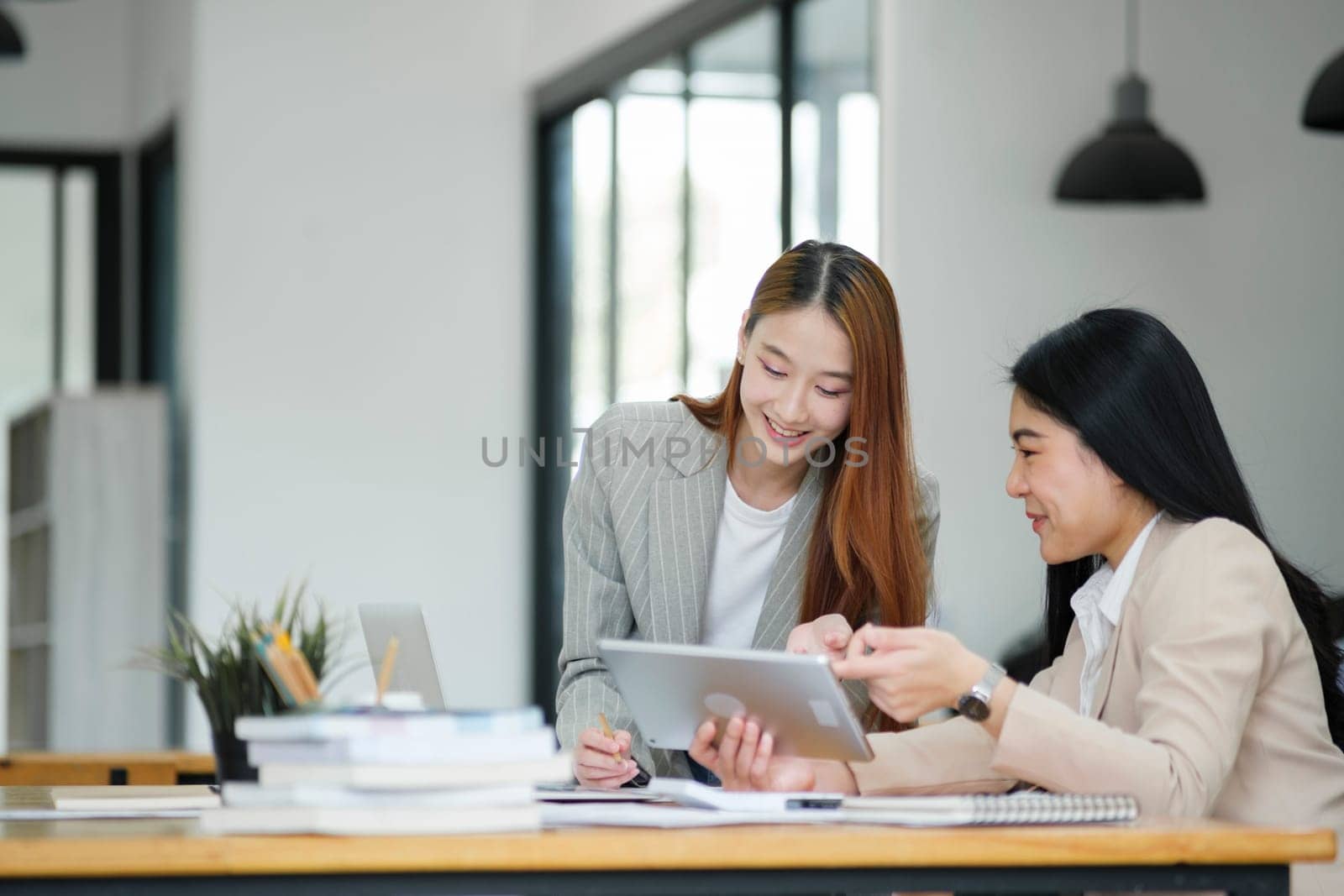 Office woman is standing and teaching a new employee. It describes the work format displayed on the tablet screen.