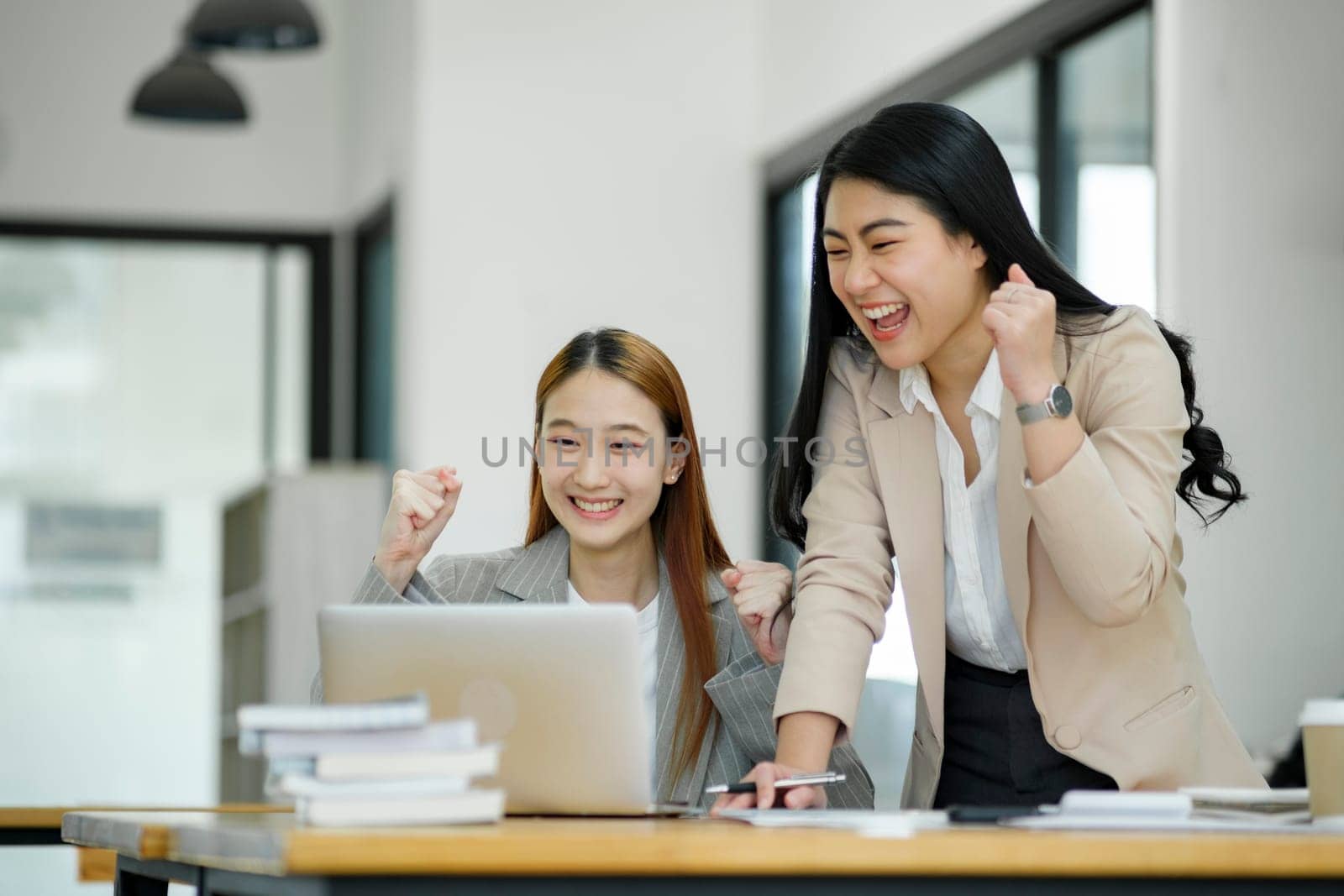 Two ecstatic businesswomen celebrating a successful moment at work with a laptop and documents on the desk..