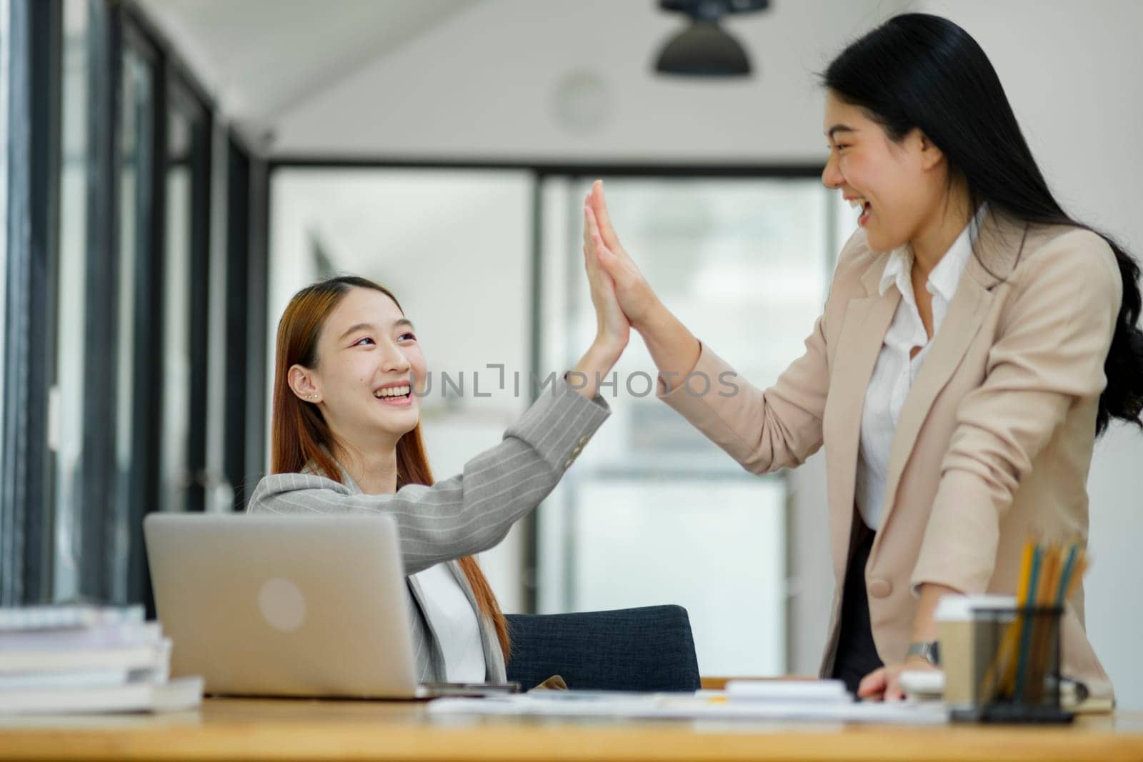 Two joyful businesswomen giving a high five in an office setting, celebrating a successful collaboration..
