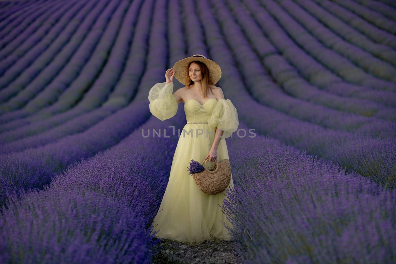Woman poses in lavender field. Happy woman in yellow dress holds lavender bouquet. Aromatherapy concept, lavender oil, photo session in lavender.