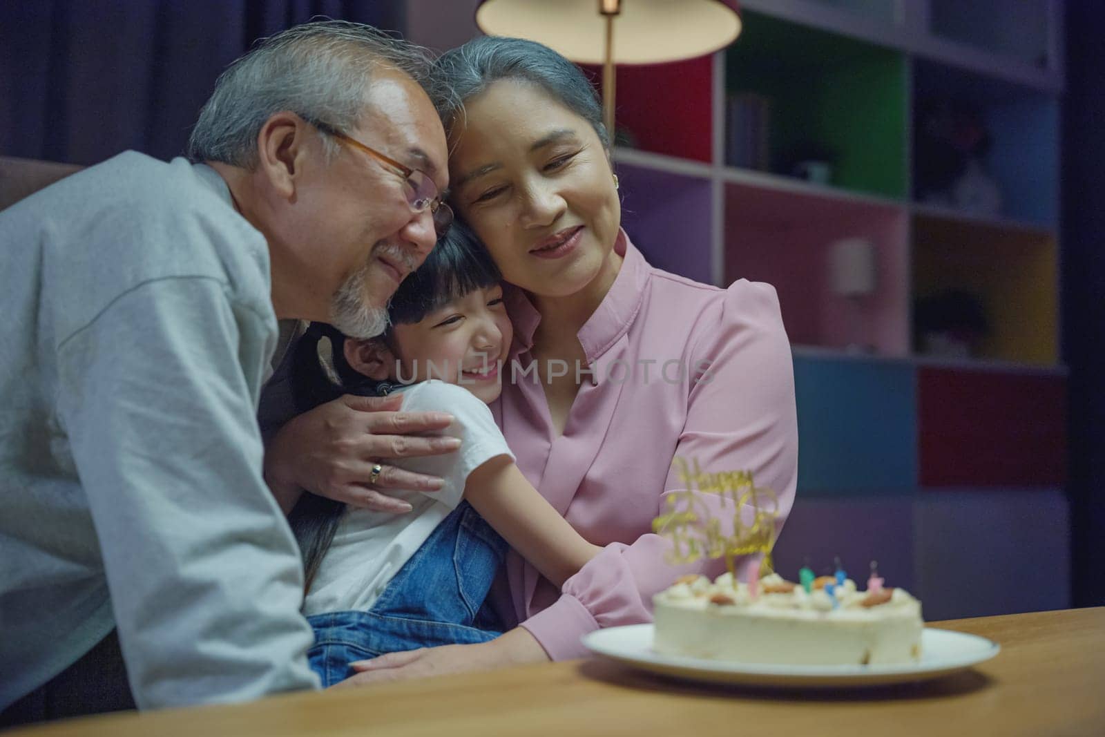 Family grandfather and grandmother hugging granddaughter feeling thankful while celebrating his birthday by Sorapop