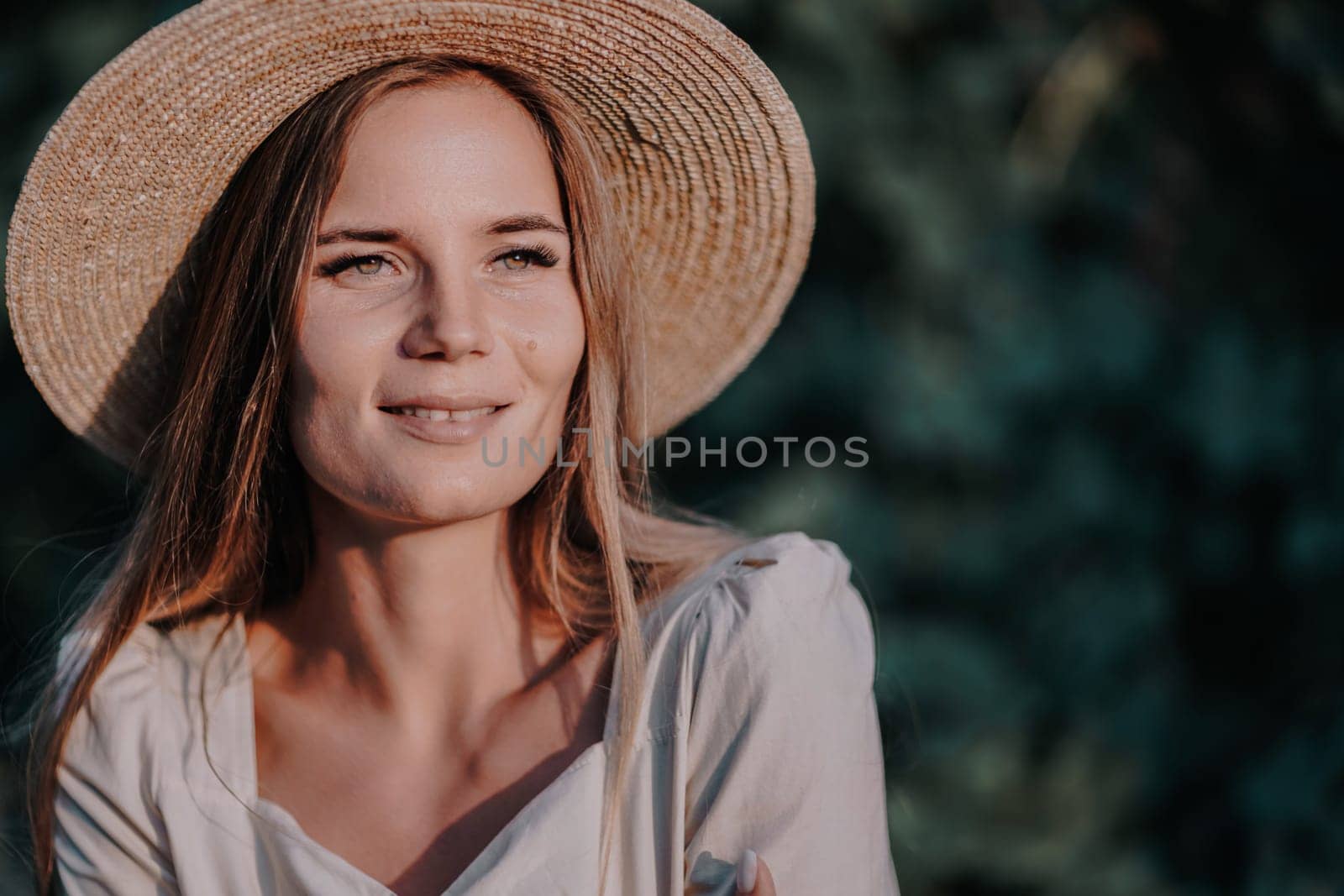 Woman with straw hat stands in front of vineyard. She is wearing a light dress and posing for a photo. Travel concept to different countries.