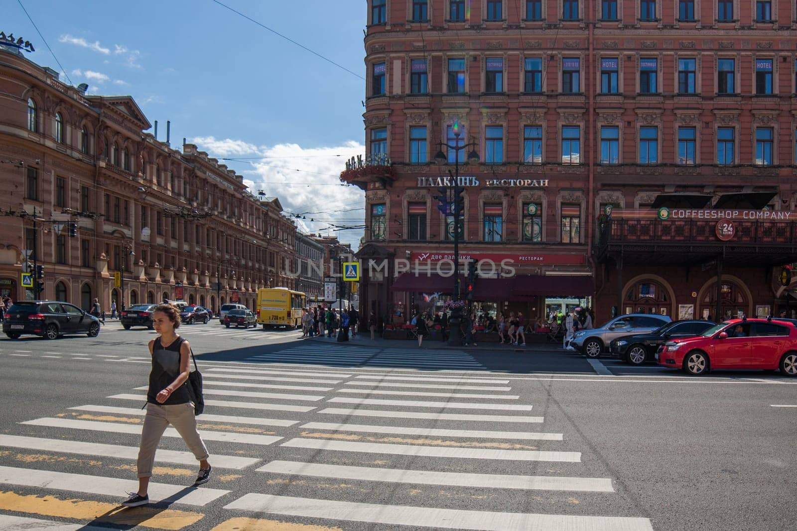 young adult Caucasian woman with black shoulder bag and back jerkin crossing street at sunny day in Saint-Petersburg, Russia: July 25, 2015