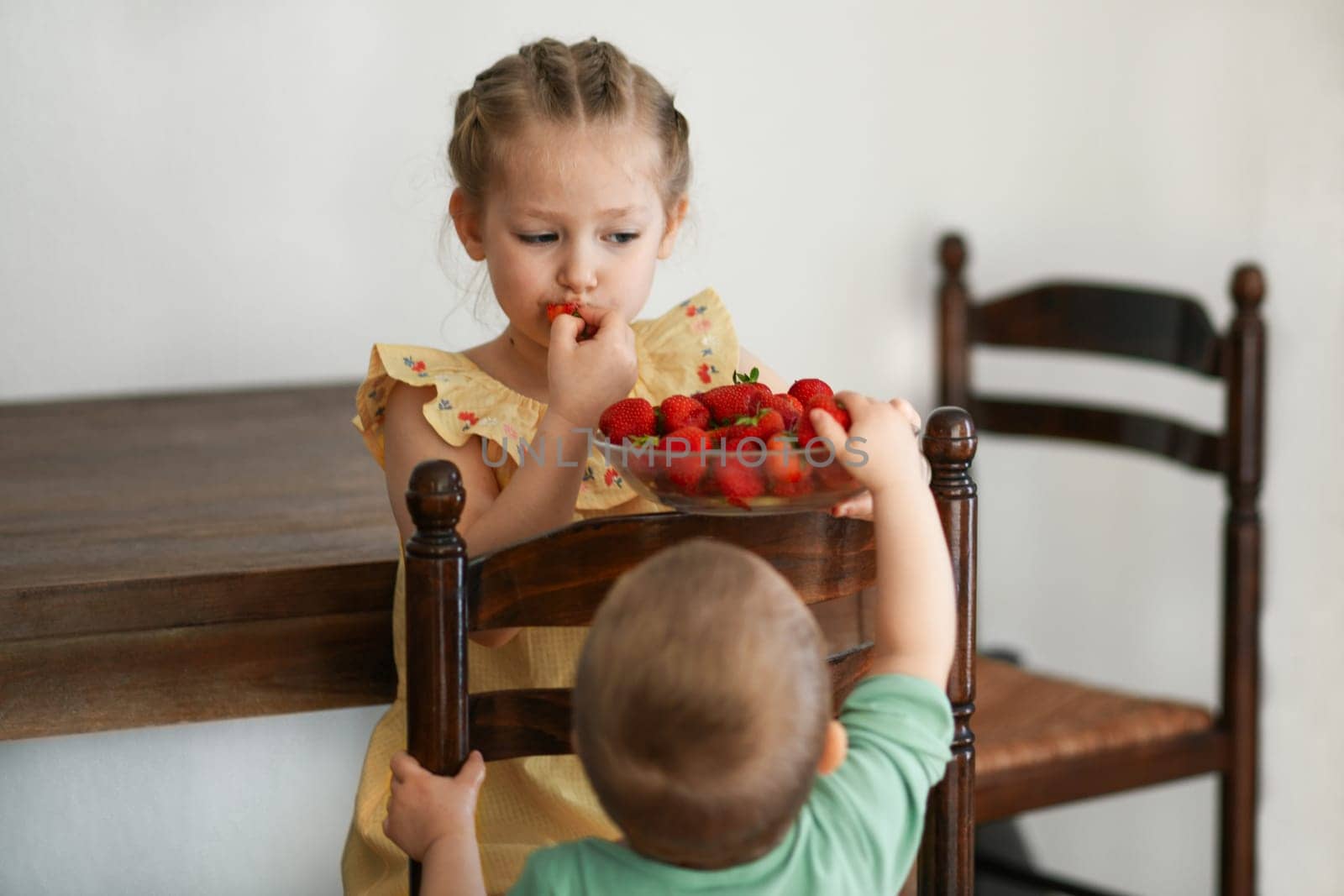 Two young girls eating strawberries in living room by Godi