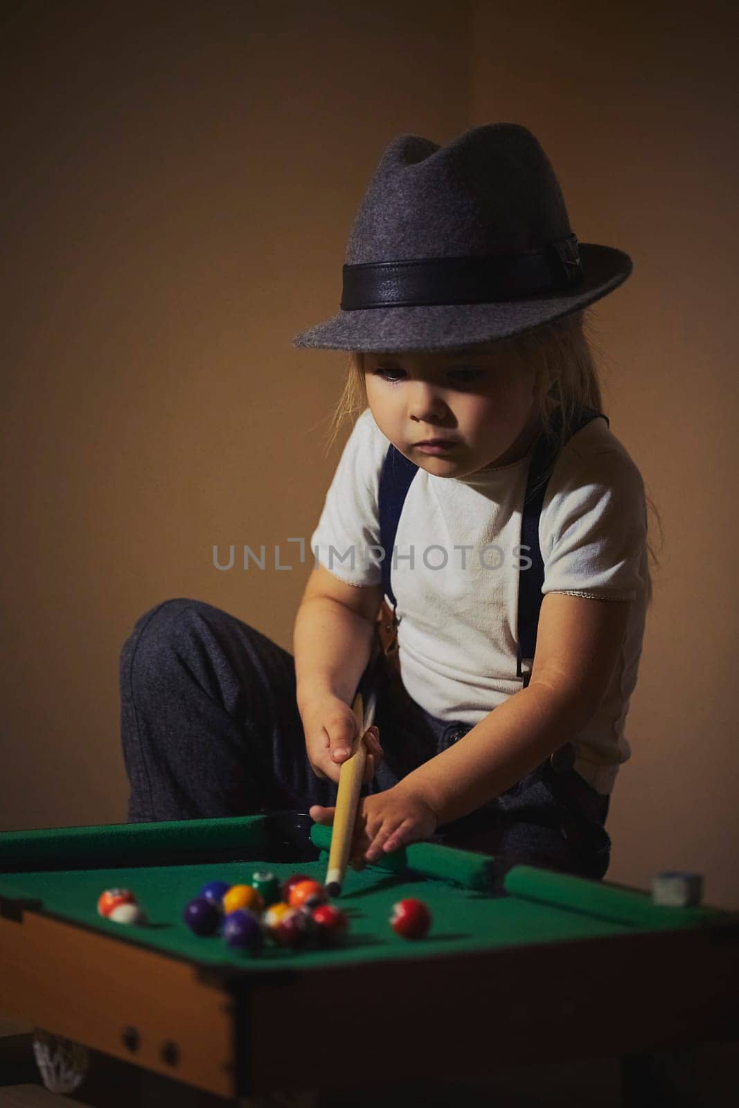 Charming child in retro clothes playing toy billiards.