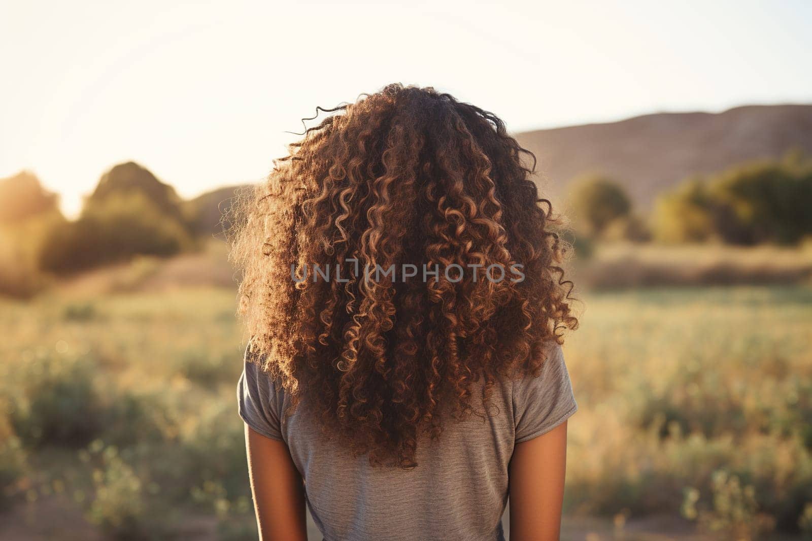 An attractive dark-skinned young woman with curly hair stands backwards in the nature.