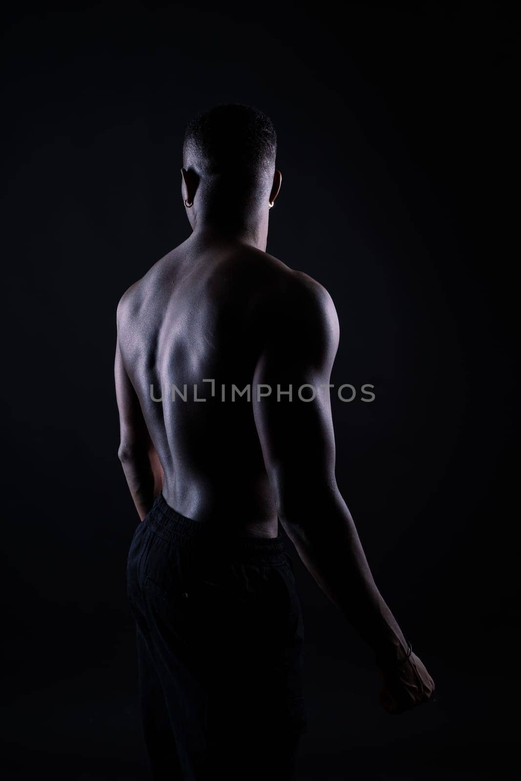 One young african muscular build man standing topless silhouette isolated on black background by Zelenin