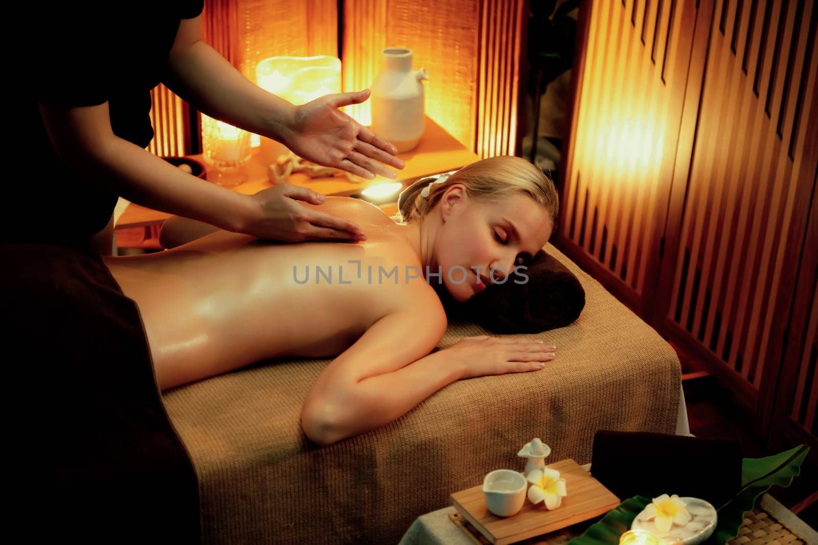 Caucasian woman customer enjoying relaxing anti-stress spa massage and pampering with beauty skin recreation leisure in warm candle lighting ambient salon spa at luxury resort or hotel. Quiescent