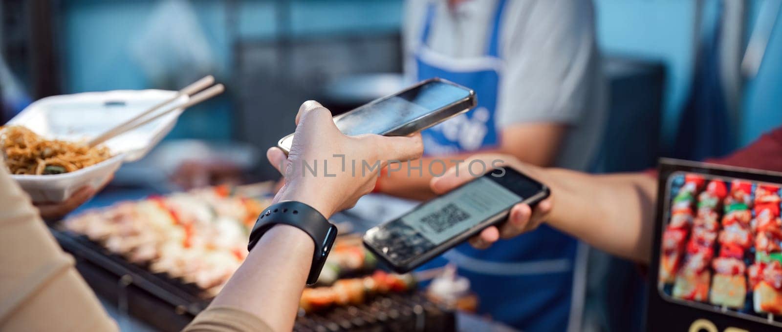 Asian traveler paying contactless with mobile phone in street food night market. Mobile payment concept.