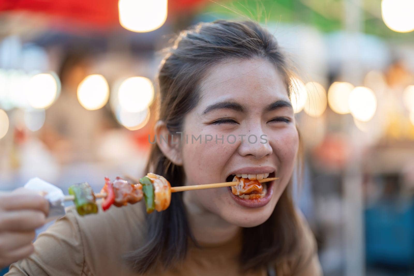 Happy young Asian Traveler foodie woman enjoy eating bbq grilled skewers at outdoor night market street food vendor.