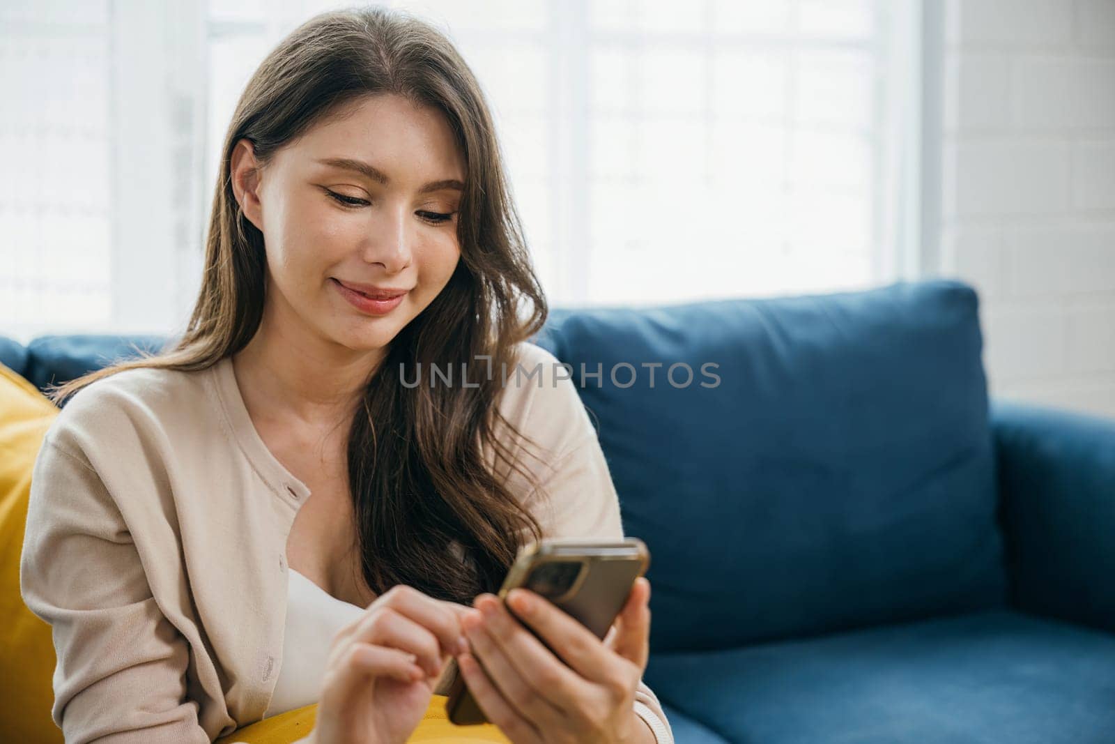 Seated comfortably a woman on a sofa talks on her phone typing messages. Amid home relaxation she finds success in communication and technology displaying a content smile. The woman is relaxing.