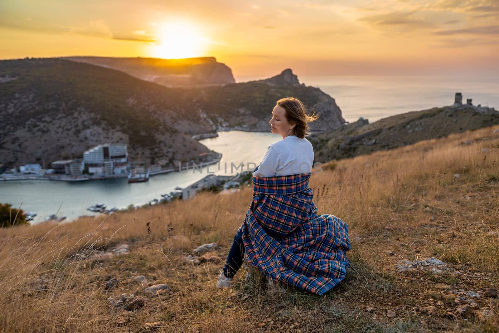 Happy woman on sunset in mountains. Woman siting with her back on the sunset in nature in summer. Silhouette. by Matiunina