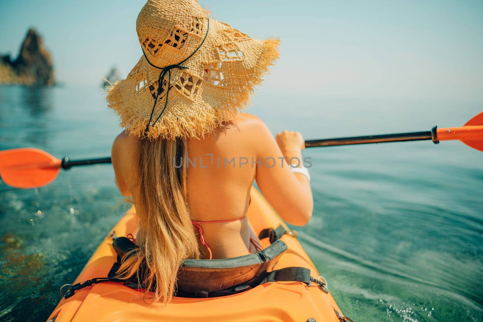 Woman in kayak back view. Happy woman with long hair in a swimsuit and hat floating in kayak on the sea. Summer holiday vacation. Summer holidays vacation at sea