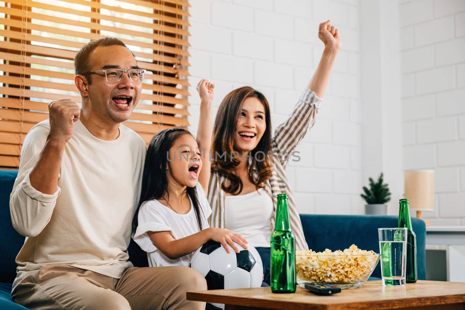With popcorn in hand, a family of fans watches a football match on TV, fostering togetherness and excitement. Their cheers and laughter capture the joy of the game and celebrating a triumph.