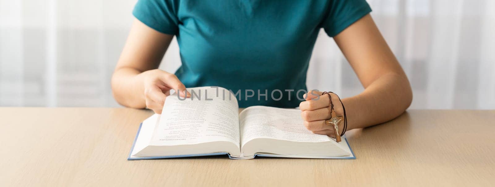 Female believer reads holy bible faithfully while holding cross at light wooden church. Concept of hope, religion, faith, believe, christianity, catholic and god blessing. Front view. Burgeoning.