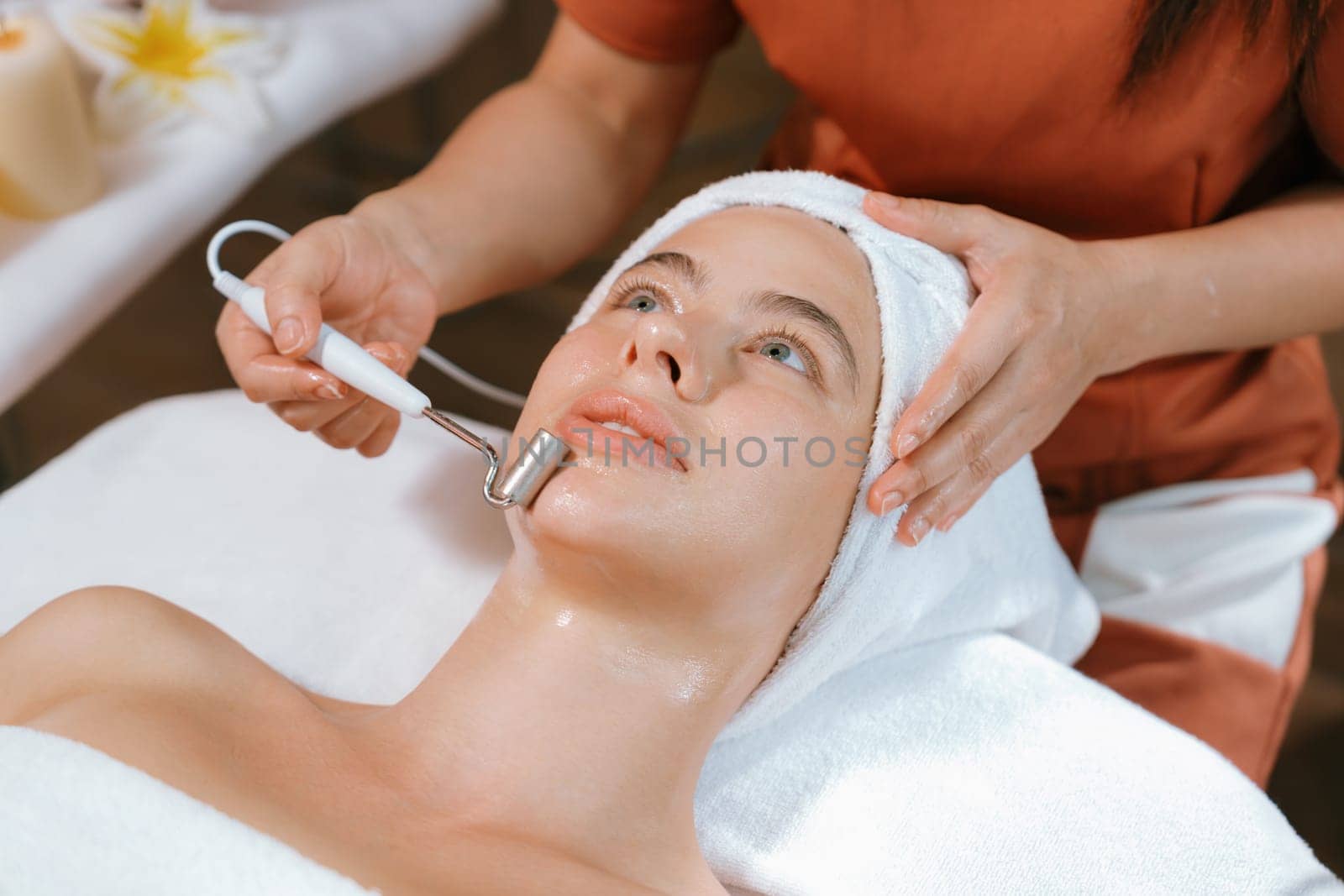 Beautiful caucasian woman lies on spa bed during having facial massage by professional hands at modern spa salon surrounded by beauty electrical equipment or medical equipment. Close up. Tranquility