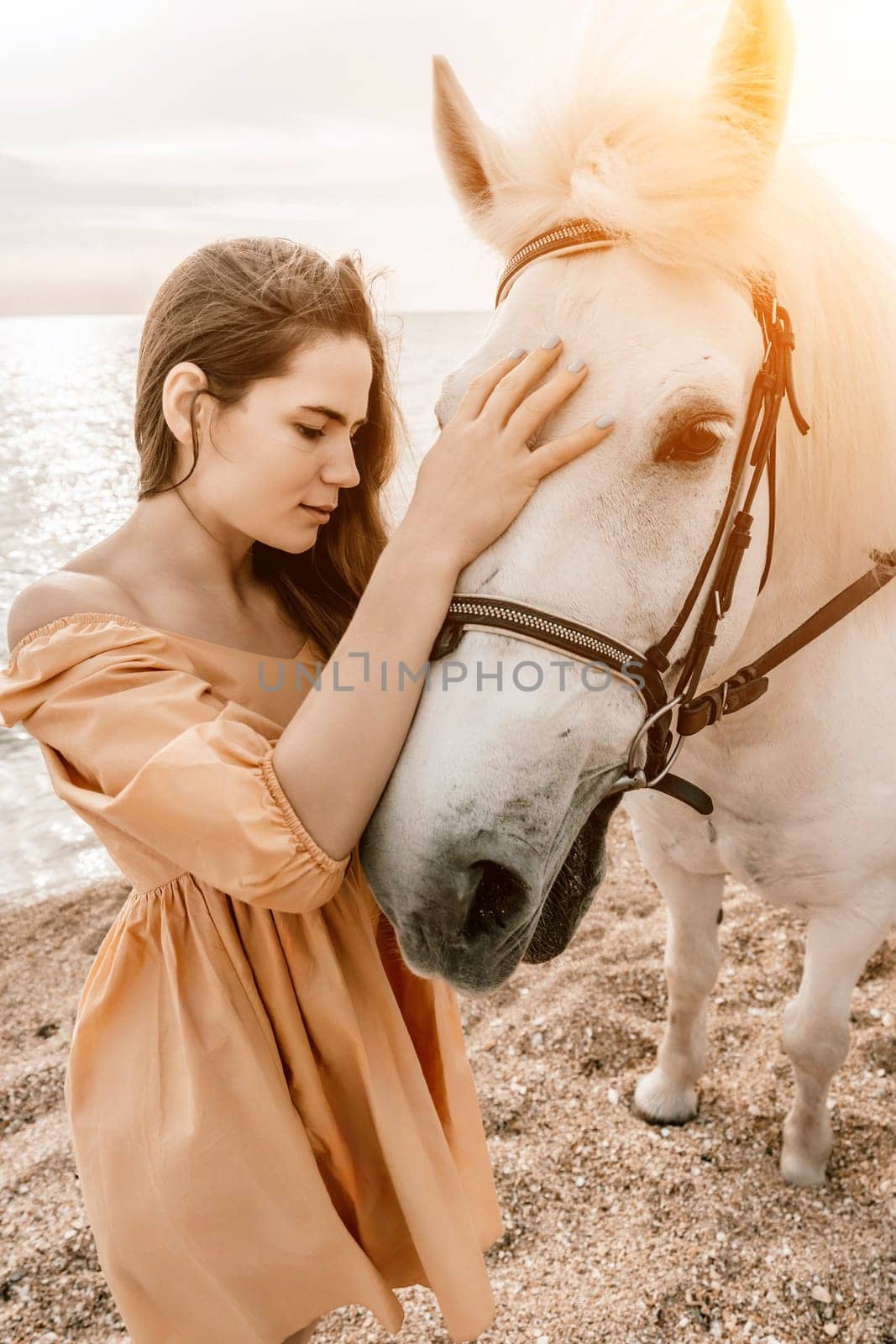 A white horse and a woman in a dress stand on a beach, with the sky and sea creating a picturesque backdrop for the scene