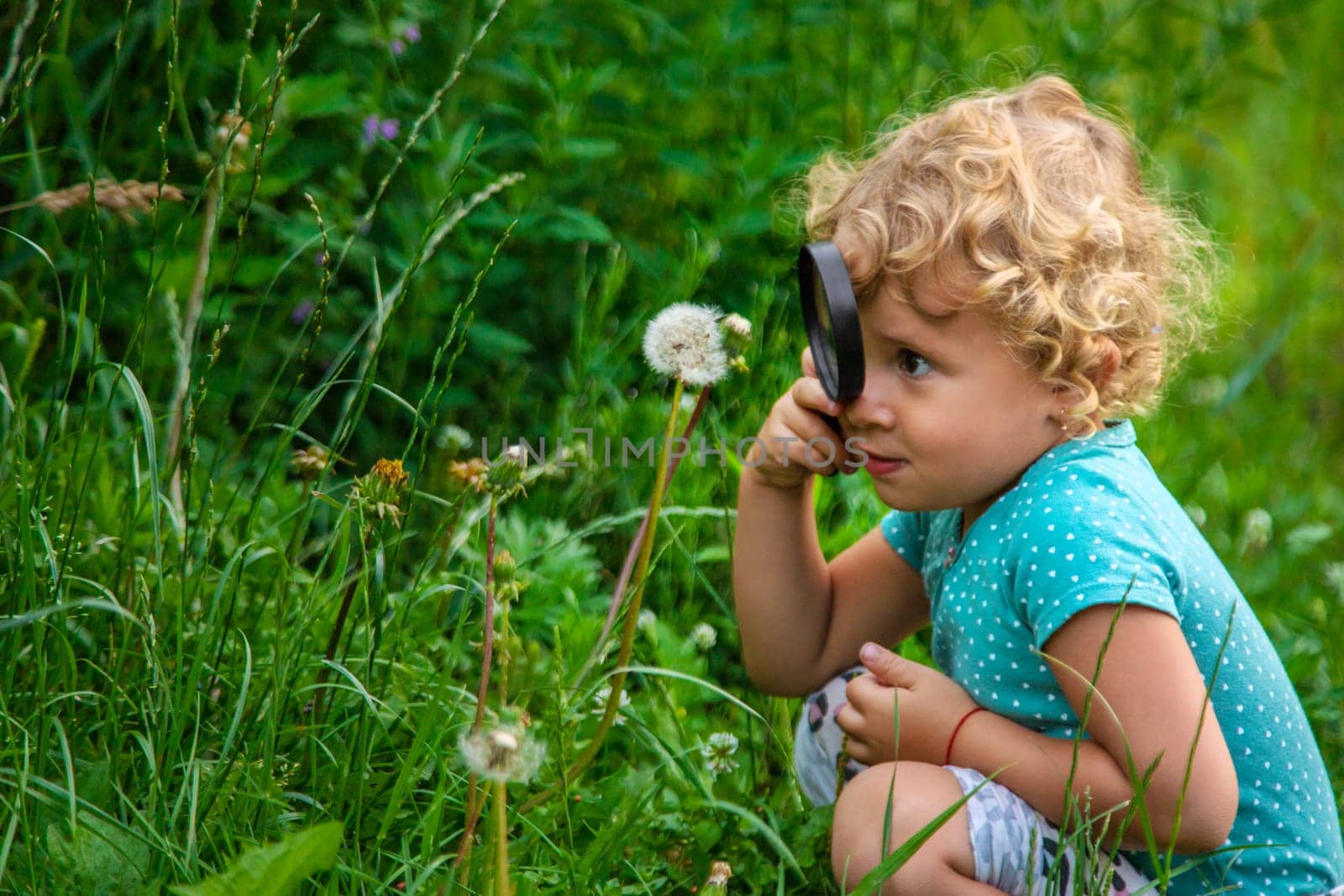 A child looks through a magnifying glass in nature. Selective focus. Kid.