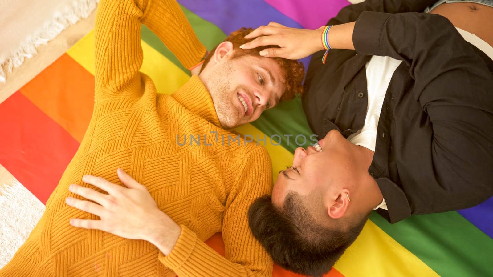 Happy gay couple smiling while lying on top of a lgbt flag