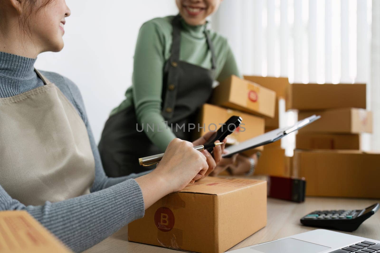 Asian woman write parcel box to prepare and using mobile for delivery to customer. e-business concept.