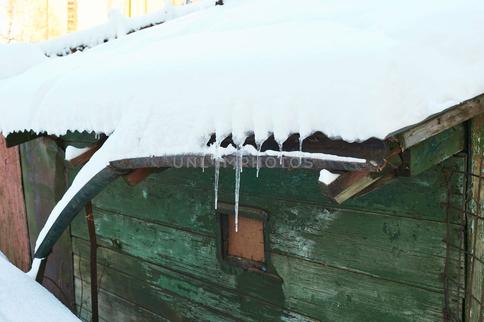 Photo an old green wooden house under the snow. Icicles on the roof.