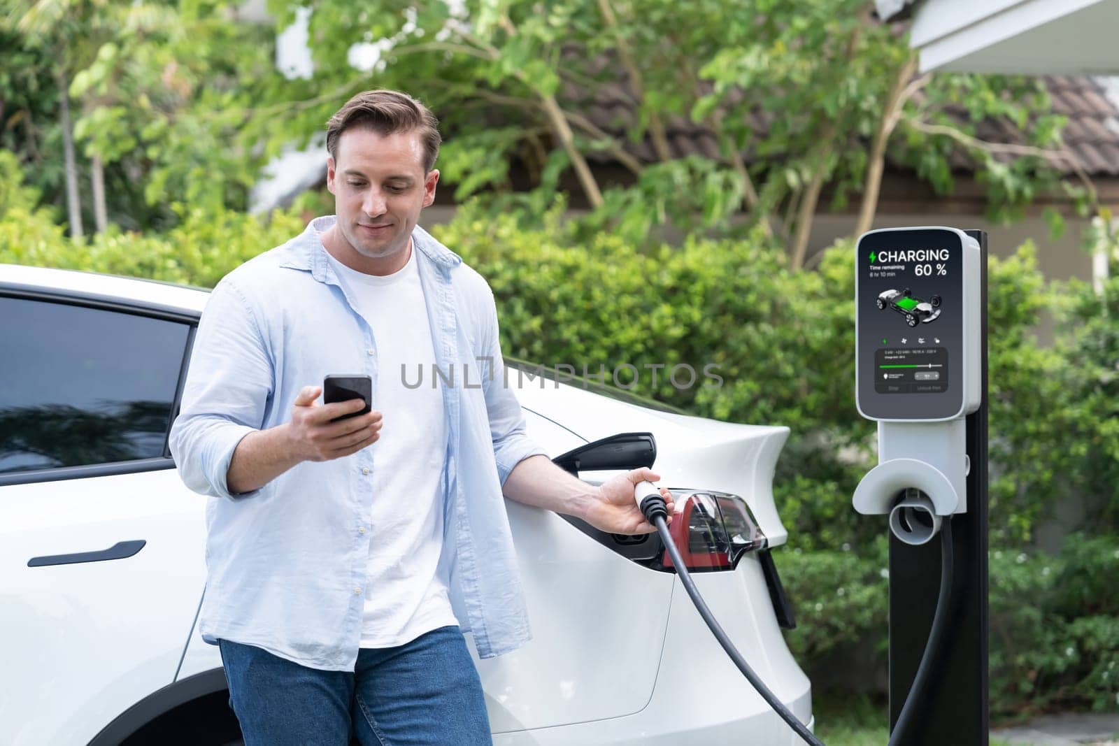 Modern eco man recharge EV car at home with phone. Synchronos by biancoblue