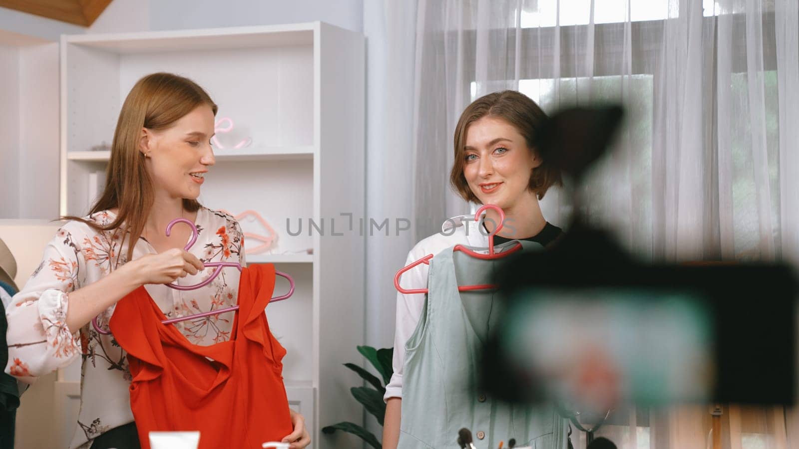 Two women influencer shoot live streaming vlog video review clothes prim social media or blog. Happy young girl with apparel studio lighting for marketing recording session broadcasting online.