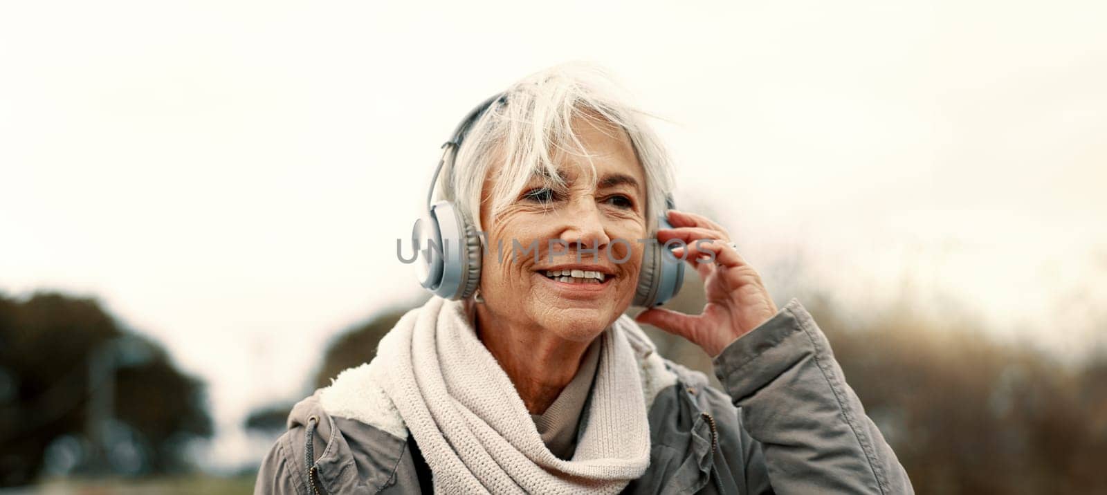 Old woman, headphones and listening to music outdoor, walking and wellness with audio streaming and energy. Podcast, radio and sound with female person on city bridge, exercise and travel with tech.