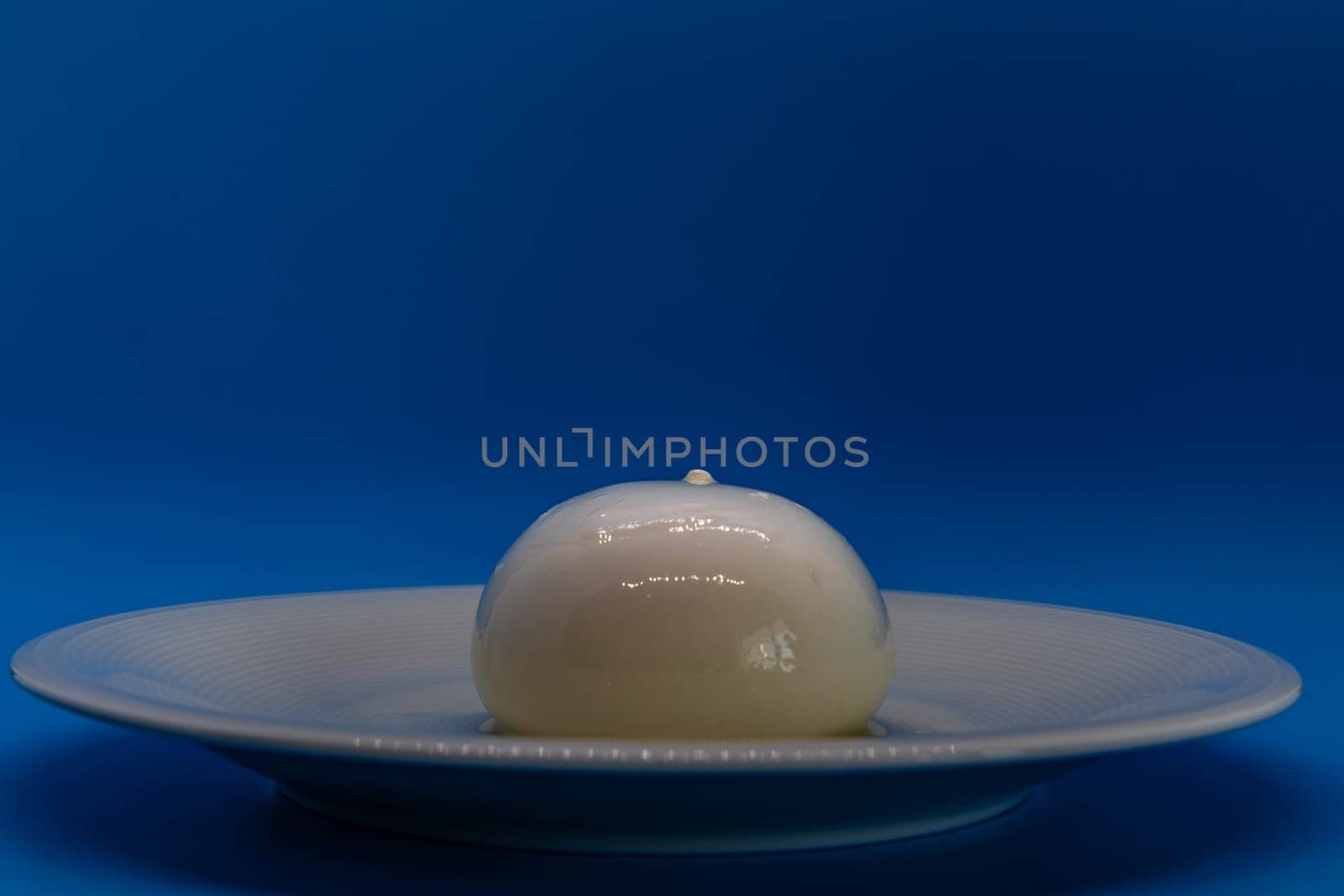 A burrata cheese rests delicately on a white plate against a vivid blue background.