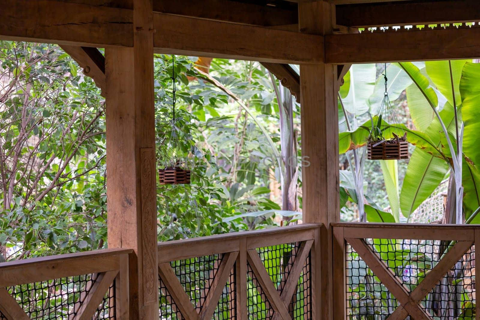 Amidst a lush forest, a charming wooden gazebo adorned with hanging baskets stands tall, inviting visitors to escape into the natural beauty of its surroundings