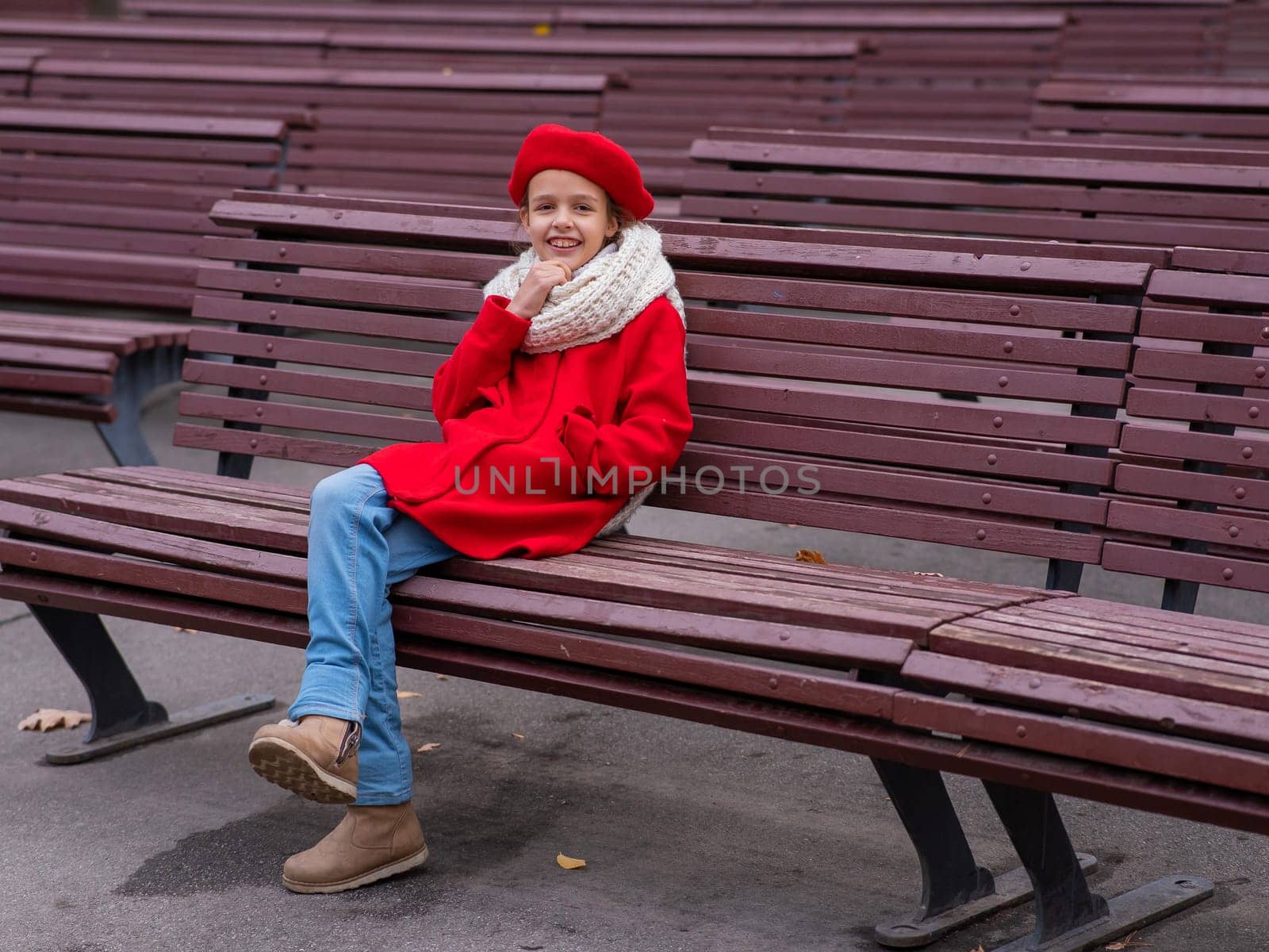 A pensive Caucasian girl in a red coat and beret sits on a bench