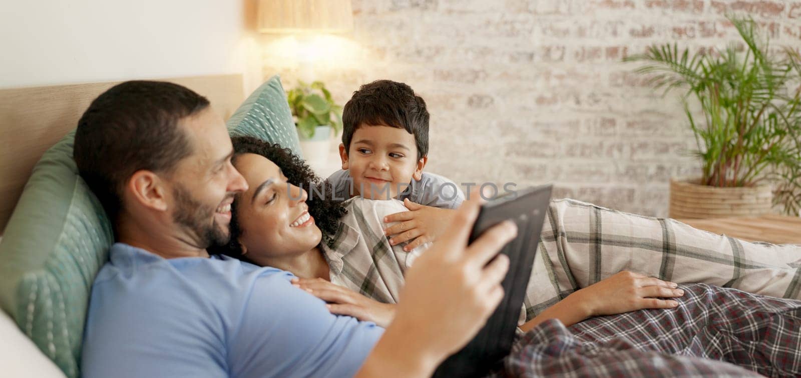 Family, bed and watching on tablet with a smile and cartoon with mom, dad and kid together. Bedroom, tech and education children program with mother, father and young boy with a youth movie at home.