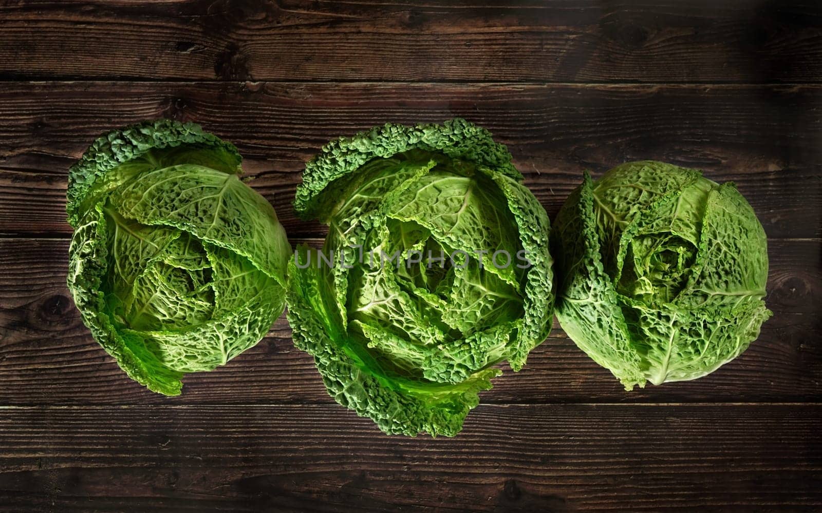 Three savoy cale cabbage heads on dark wooden board, view from above