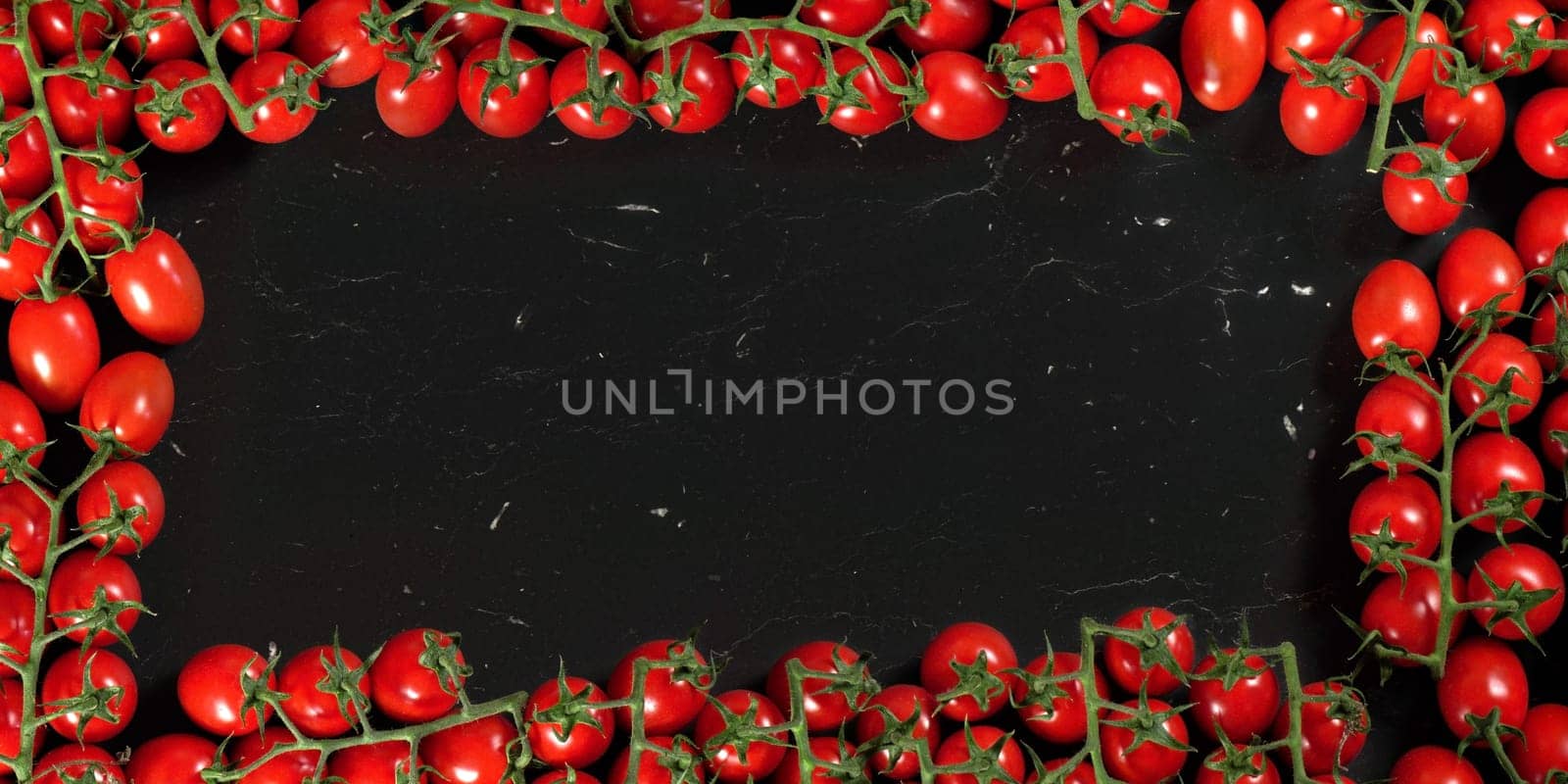 Border frame made out of tomatoes with green vine leaves, empty space left for text on black marble like board.