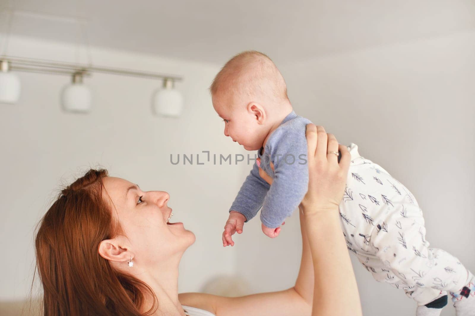 Mother playing with his infant son, holding him in her hands above her head, looks like fly