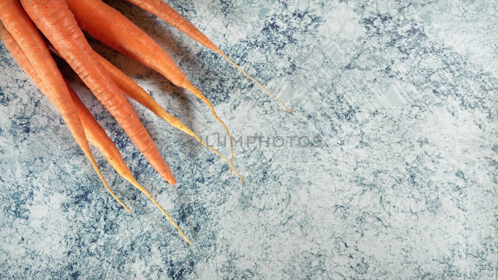 Fresh carrot roots on blue stone marble like board, wide banner with space for text right side by Ivanko