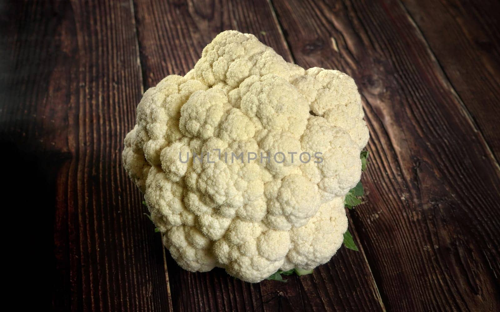 Closeup on whole white raw cauliflower vegetable on dark wooden board