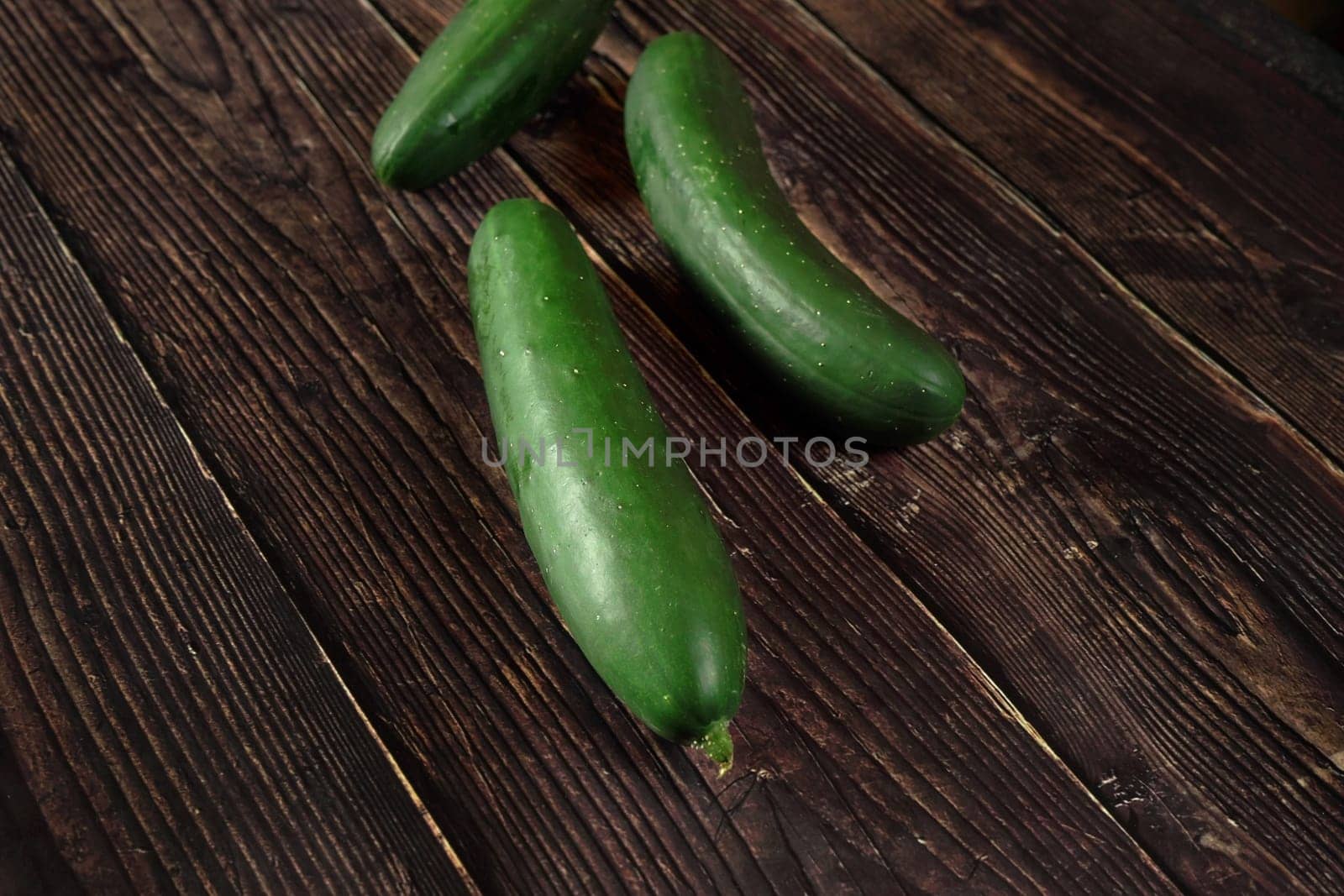 Dark green whole raw cucumbers on old rustic wooden table by Ivanko